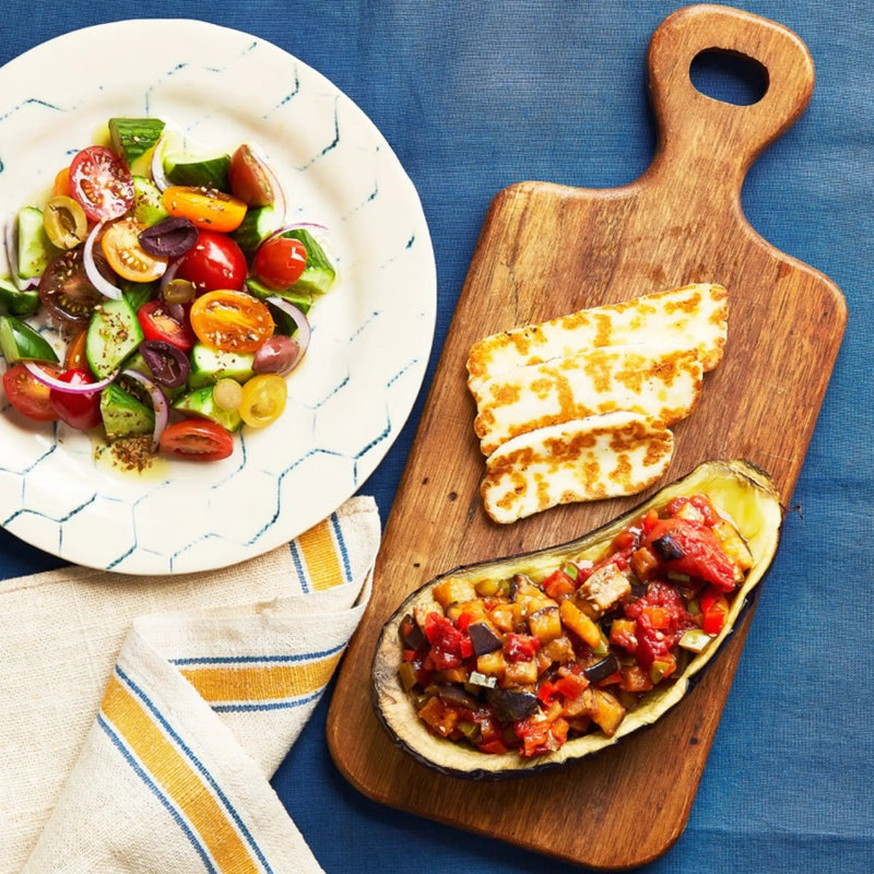 A closeup of a tray with Aubergine & Halloumi Bake on a blue tablecloth for upcoming menu provided by Laroot World, an organic, local, gluten free New York City flexitarian, pescatarian, carnitarian, vegan, and vegetarian meal delivery service 